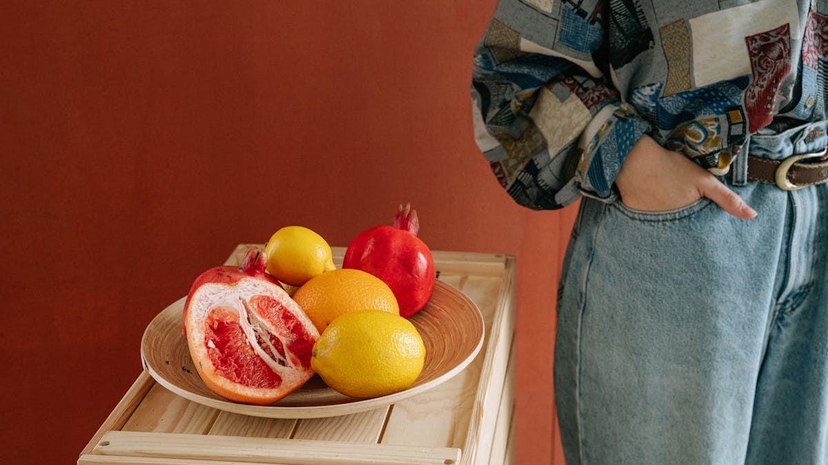 Vibrant citrus fruits displayed on wooden tray next to casual person indoors.